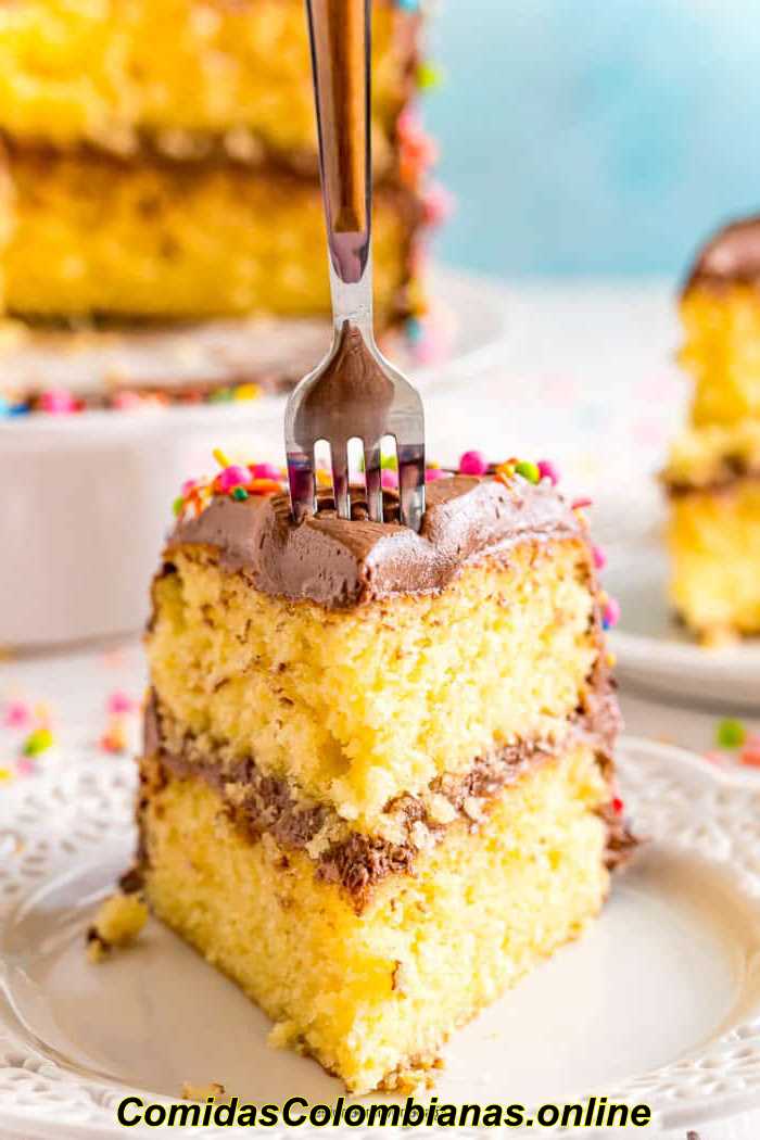 포크는 하얀 접시에 초콜릿 설탕을 입힌 노란색 케이크 한 조각에 담근다.