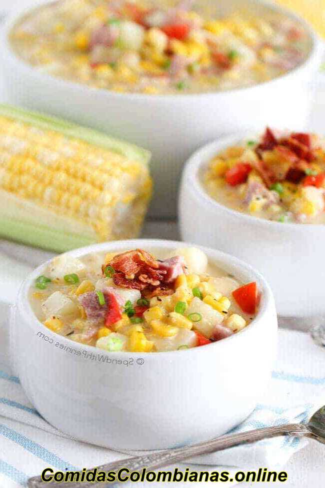 Dos tazones blancos de sopa de jamón y maíz con una mazorca de maíz y un tazón más grande al fondo