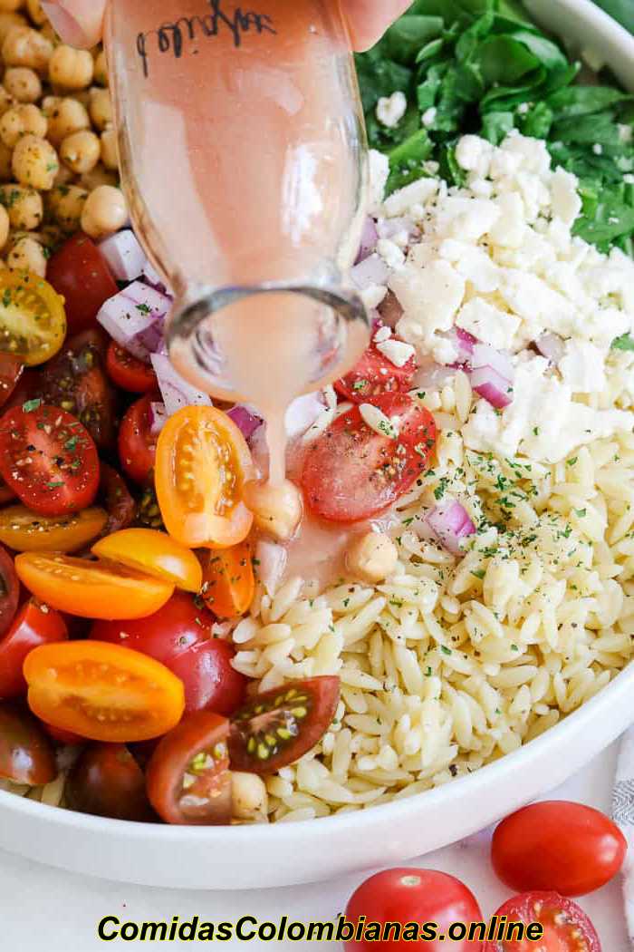 Despeje o molho sobre a salada de macarrão Orzo com tomate, espinafre e grão de bico em uma tigela
