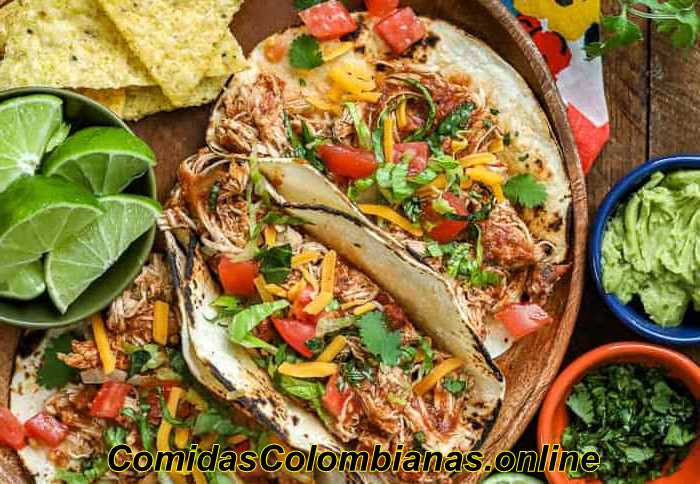 Tacos di pollo Crock Pot su un piatto di legno con ingredienti taco e coriandolo