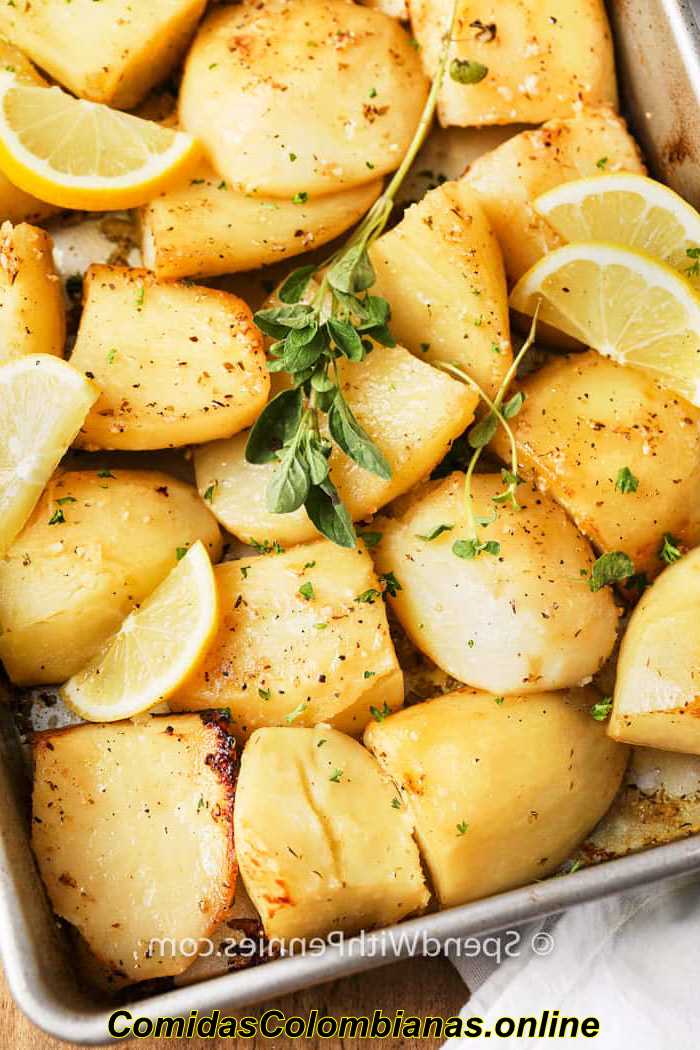 Patatas asadas con limón al estilo griego en una bandeja para hornear con tomillo y gajos de limón