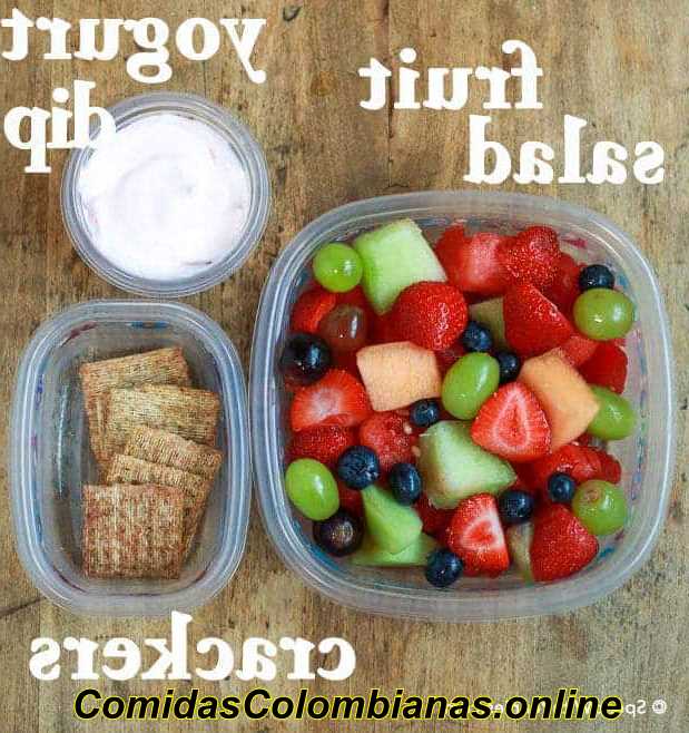 Fotografía cenital de salsa de yogur, ensalada de frutas y galletas saladas
