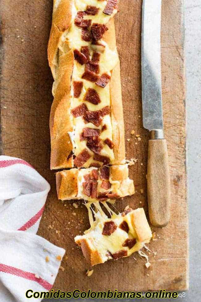 Photo aérienne d'une baguette remplie de sauce à pizza sur une planche à découper à côté d'un couteau à pain