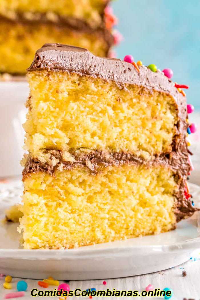 하얀 접시에 초콜릿 설탕을 입힌 노란색 케이크 한 조각의 사진을 닫습니다.