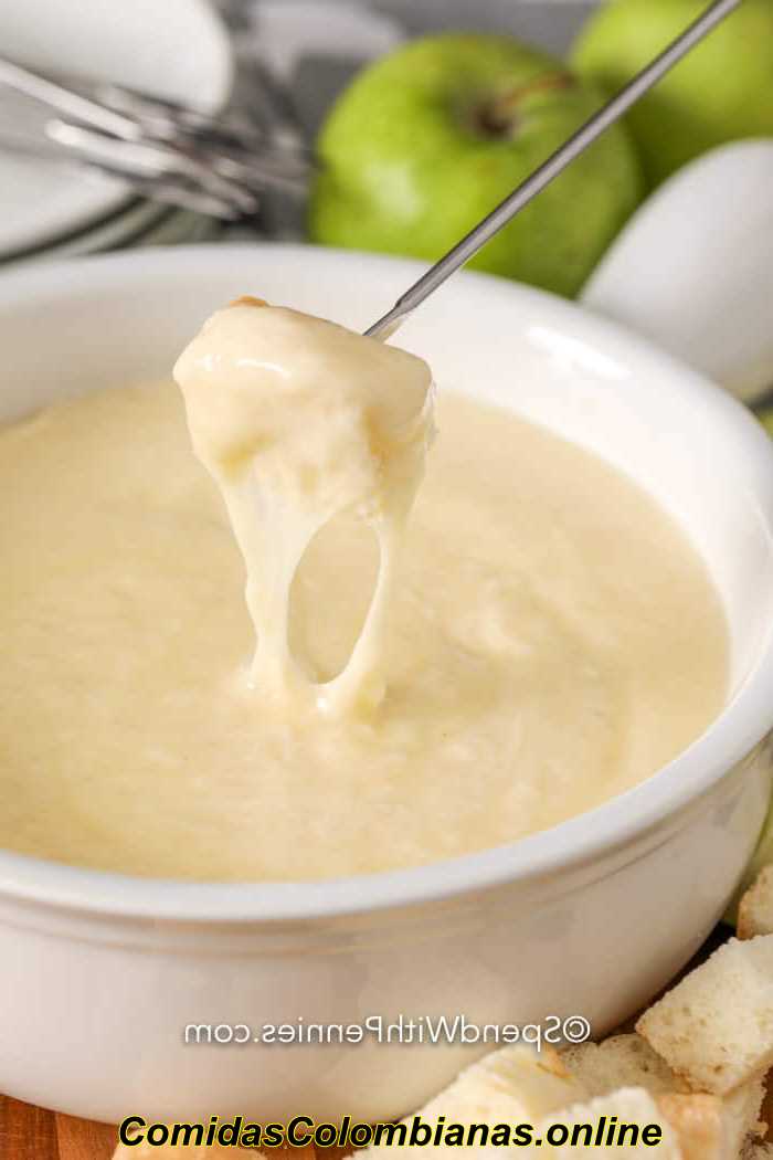Fondue de queso en un tazón blanco sumergido con pan de un pincho de fondue